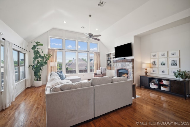 living area featuring lofted ceiling, a fireplace, visible vents, ceiling fan, and wood finished floors