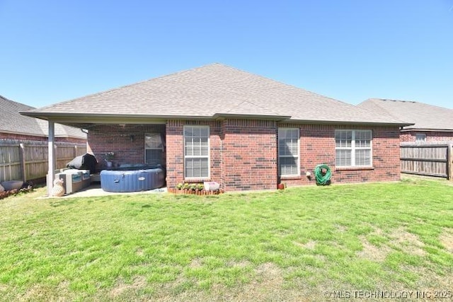 back of house featuring a yard, brick siding, a fenced backyard, and a hot tub