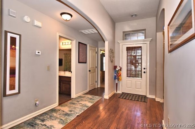 entrance foyer with dark wood-style flooring, visible vents, baseboards, and arched walkways