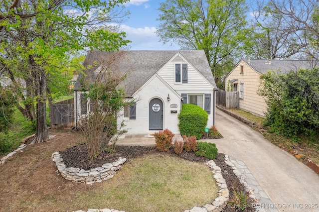 view of front facade featuring brick siding, fence, and roof with shingles
