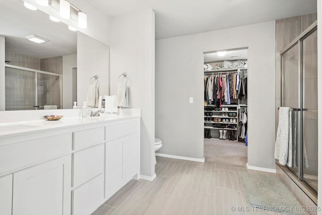 bathroom with a shower stall, a spacious closet, vanity, baseboards, and toilet