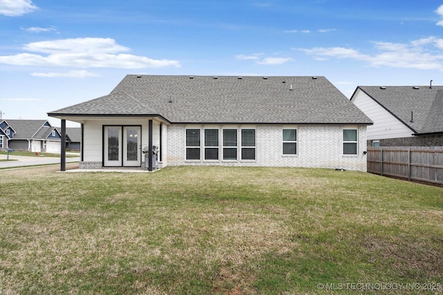 back of property featuring brick siding, a lawn, a shingled roof, and fence