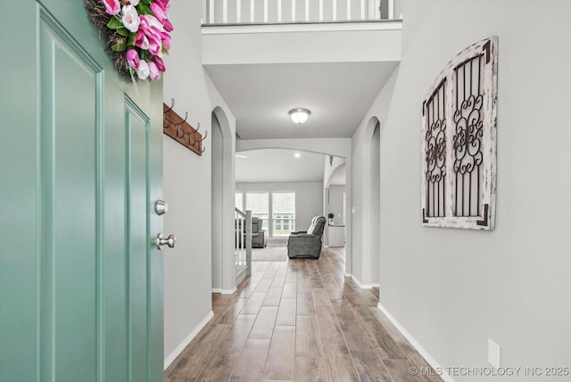 entryway with arched walkways, wood finished floors, and baseboards