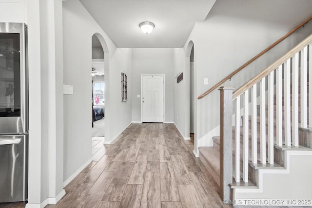 foyer with baseboards, wood finished floors, arched walkways, and stairway
