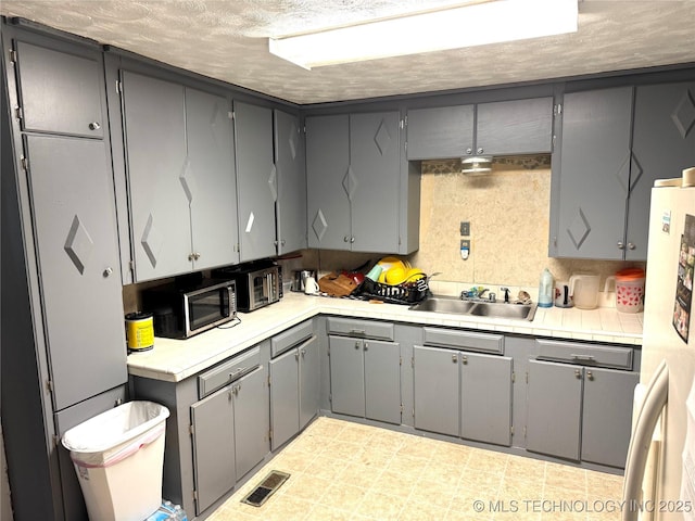 11847 Weaverville Ln, Kingston, OK 73439 - kitchen featuring freestanding refrigerator, visible vents, gray cabinets, stainless steel microwave, and light countertops
