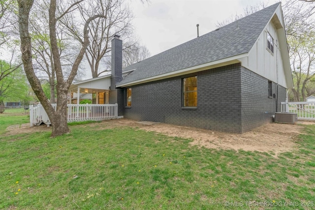 back of house with a lawn, a chimney, central air condition unit, brick siding, and roof with shingles
