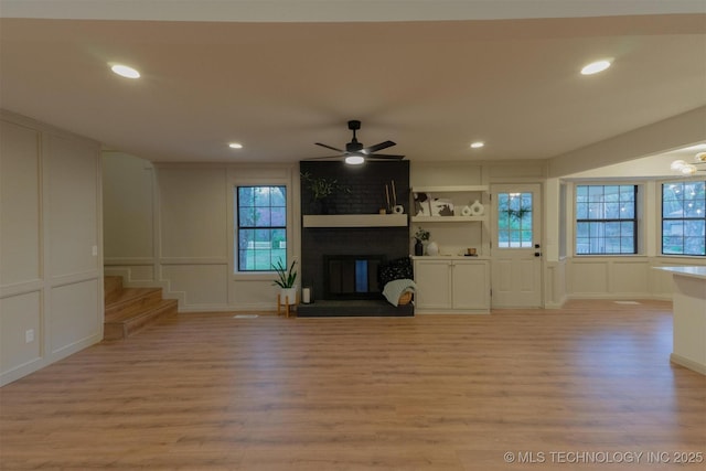 unfurnished living room with light wood-style floors, a decorative wall, ceiling fan, a brick fireplace, and stairs