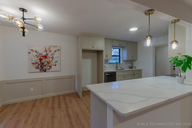 kitchen with light stone counters, light wood-style flooring, backsplash, stainless steel dishwasher, and a sink