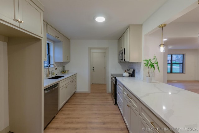 kitchen featuring a sink, appliances with stainless steel finishes, light wood finished floors, backsplash, and light stone counters