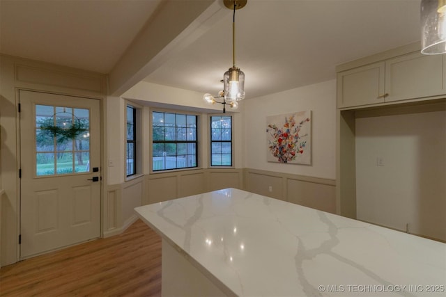 dining area featuring a decorative wall, light wood-type flooring, an inviting chandelier, and a wainscoted wall
