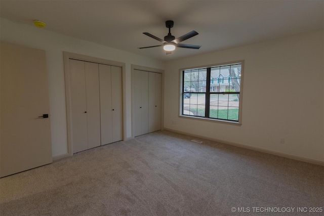 unfurnished bedroom with two closets, baseboards, a ceiling fan, and carpet
