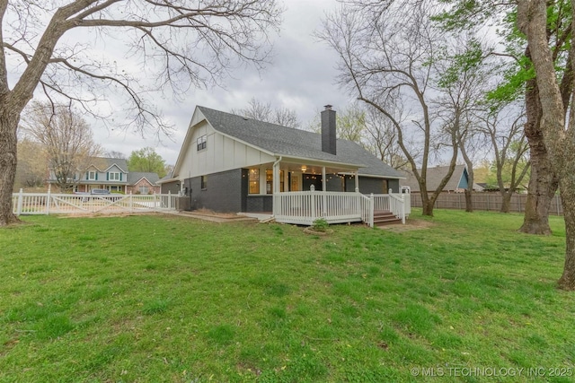 rear view of house with a deck, a fenced backyard, a chimney, and a lawn