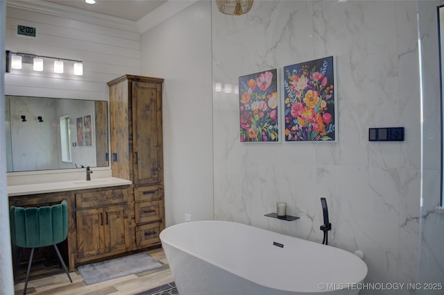 full bathroom with vanity, a freestanding bath, visible vents, ornamental molding, and wood finished floors