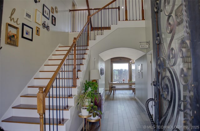 stairs with baseboards, arched walkways, and a towering ceiling