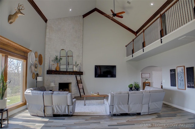 living room with arched walkways, a fireplace, wood finished floors, a ceiling fan, and high vaulted ceiling