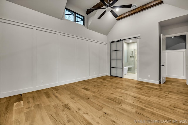 unfurnished bedroom with light wood finished floors, beam ceiling, a decorative wall, and a barn door