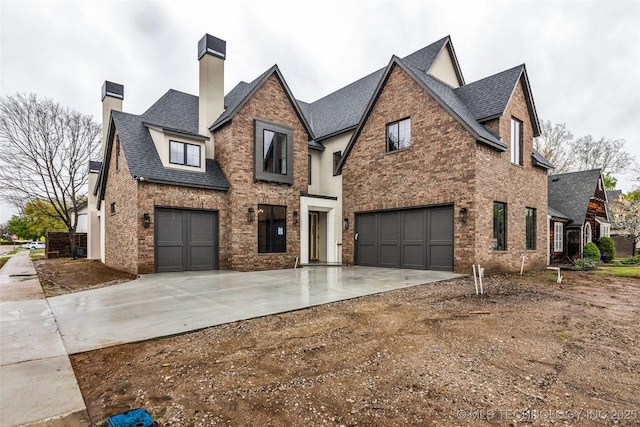 view of front of home with driveway, a chimney, brick siding, an attached garage, and a shingled roof