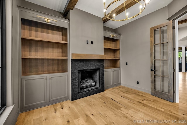 unfurnished living room featuring a high end fireplace, an inviting chandelier, light wood-style flooring, baseboards, and beam ceiling