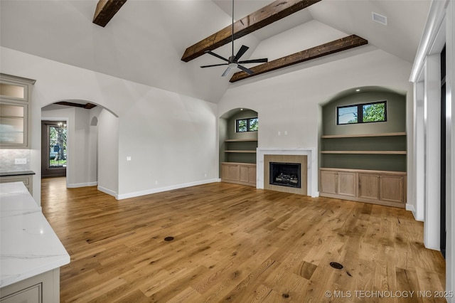 unfurnished living room featuring arched walkways, visible vents, beamed ceiling, ceiling fan, and a fireplace
