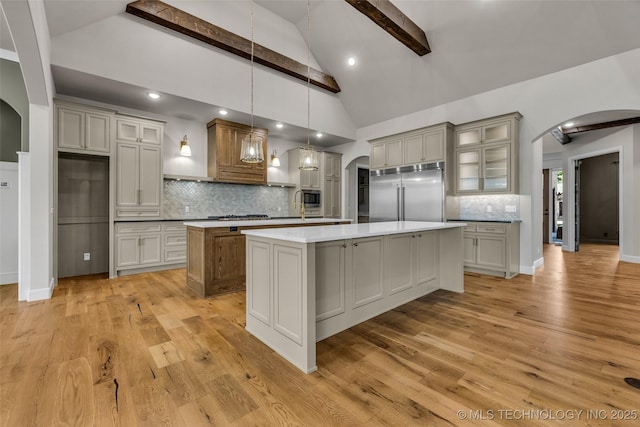 kitchen with built in appliances, decorative backsplash, arched walkways, and a spacious island