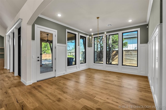unfurnished dining area with a decorative wall, crown molding, wood finished floors, an inviting chandelier, and recessed lighting
