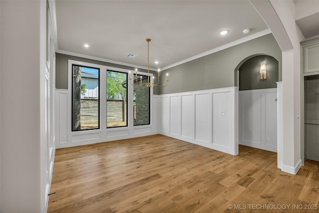 unfurnished dining area with light wood-type flooring, arched walkways, ornamental molding, and a decorative wall