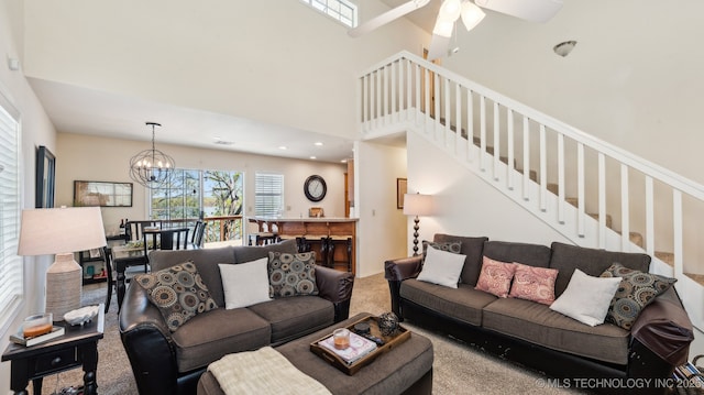living room with ceiling fan with notable chandelier, carpet flooring, a towering ceiling, and stairway