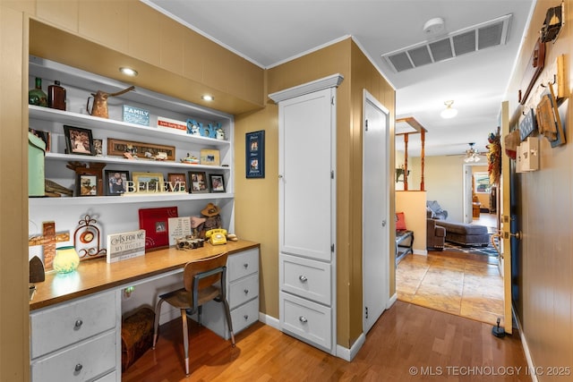 office area with crown molding, ceiling fan, light wood-type flooring, visible vents, and built in desk