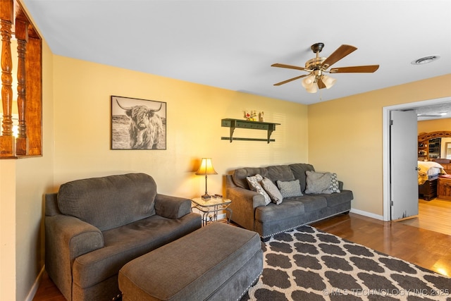 living room featuring wood finished floors, ceiling fan, baseboards, and visible vents