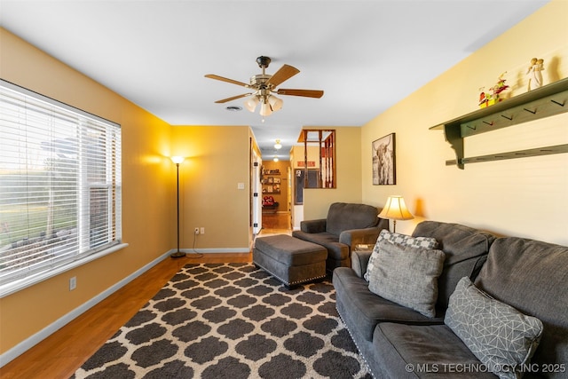 living area with baseboards, a ceiling fan, and wood finished floors