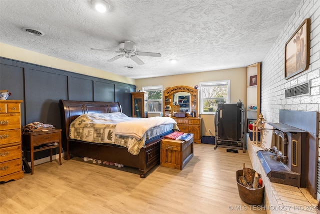 bedroom with light wood-style floors, a ceiling fan, visible vents, and a textured ceiling