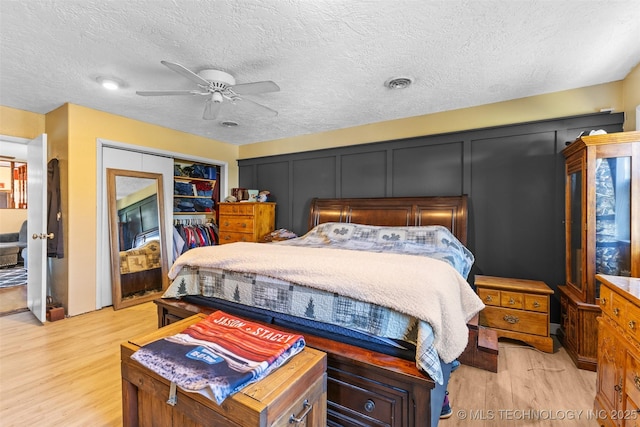 bedroom with a closet, light wood-type flooring, a textured ceiling, a ceiling fan, and visible vents