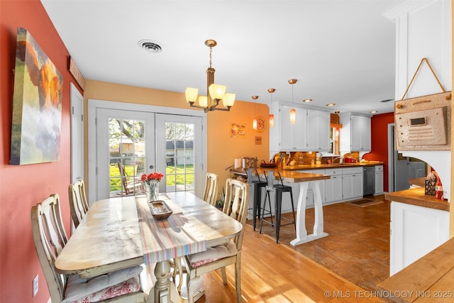 dining room with light wood finished floors, french doors, an inviting chandelier, and visible vents