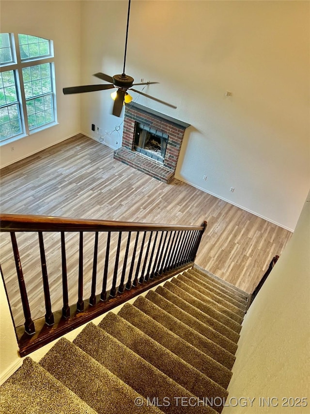 stairs with baseboards, a ceiling fan, wood finished floors, and a fireplace