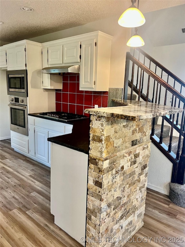 kitchen featuring light wood finished floors, under cabinet range hood, dark countertops, appliances with stainless steel finishes, and white cabinetry