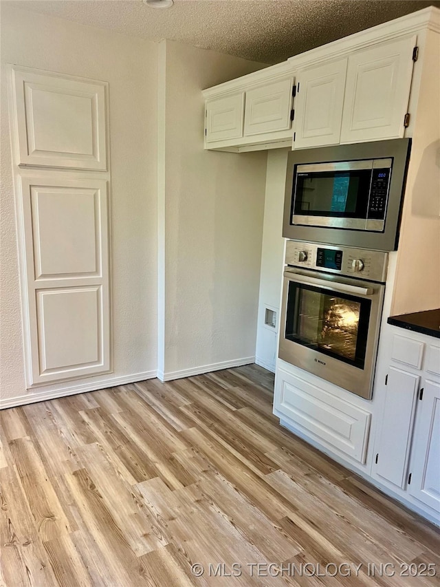 kitchen featuring white cabinets, a textured ceiling, light wood-type flooring, dark countertops, and appliances with stainless steel finishes