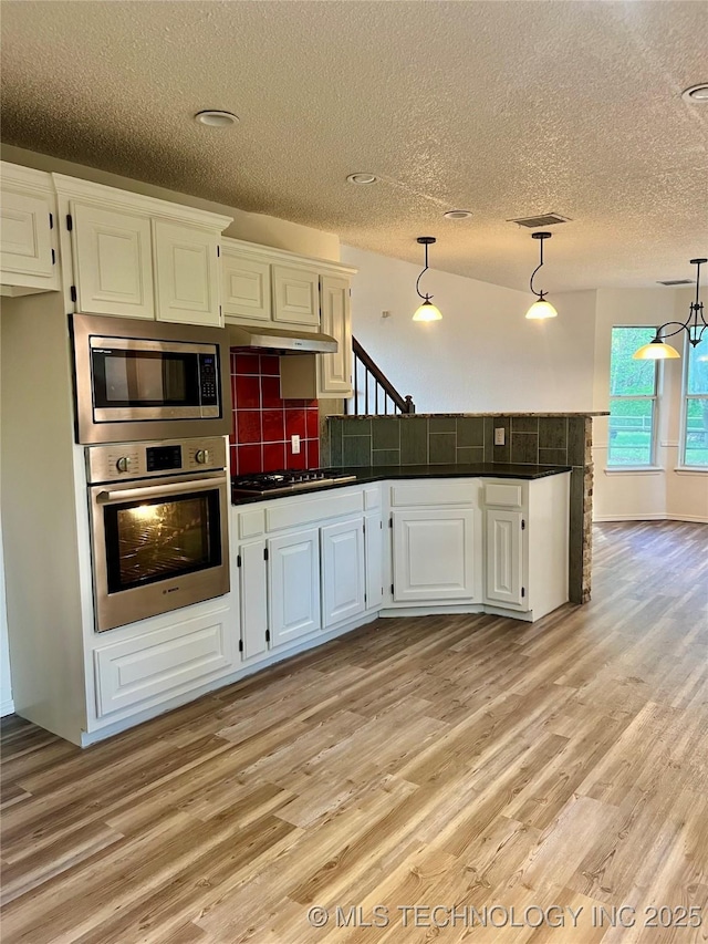 kitchen with a peninsula, light wood-style flooring, a textured ceiling, and appliances with stainless steel finishes