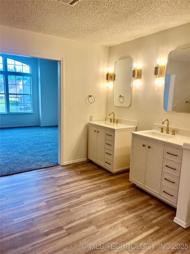 full bath featuring two vanities, wood finished floors, a sink, and a textured ceiling