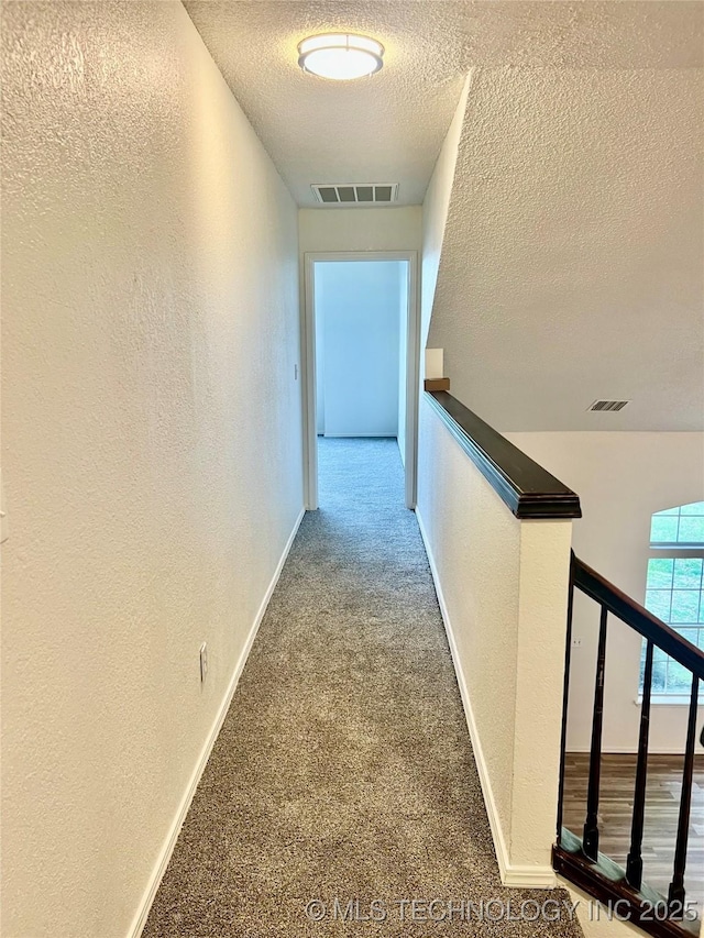 hall with a textured wall, a textured ceiling, carpet flooring, and visible vents