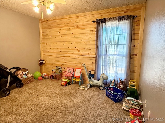 game room with wood walls, ceiling fan, a textured ceiling, and carpet floors