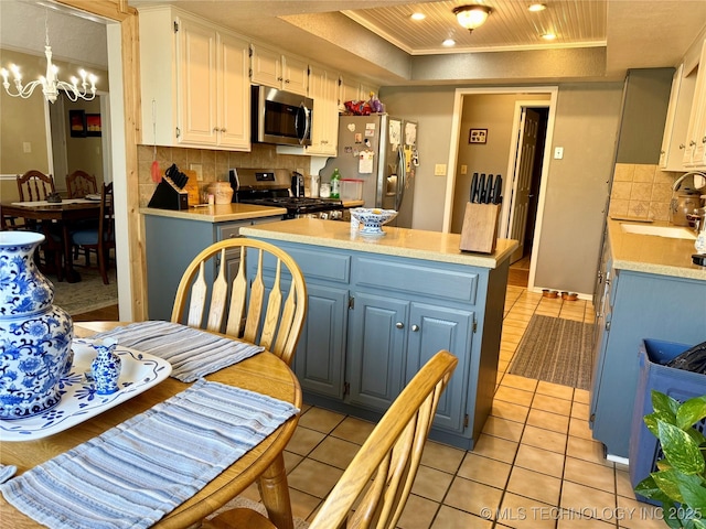 kitchen with a center island, a raised ceiling, a sink, light countertops, and stainless steel appliances