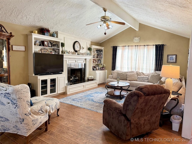 living area featuring a textured ceiling, ceiling fan, wood-type flooring, and vaulted ceiling with beams