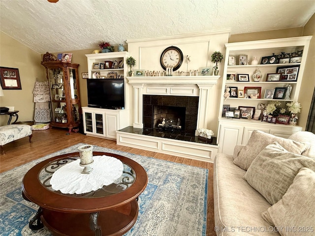 living room with a tiled fireplace, lofted ceiling, a textured ceiling, and wood finished floors