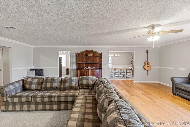 living area with crown molding, wood finished floors, ceiling fan with notable chandelier, and visible vents