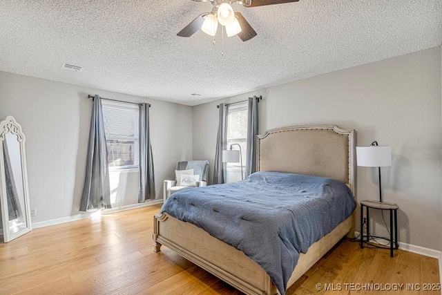 bedroom featuring ceiling fan, a textured ceiling, visible vents, wood finished floors, and baseboards
