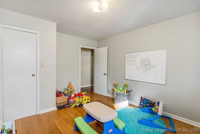 recreation room featuring baseboards, wood finished floors, and a textured ceiling