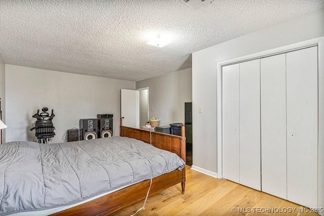 bedroom featuring light wood-style flooring, a closet, a textured ceiling, and visible vents