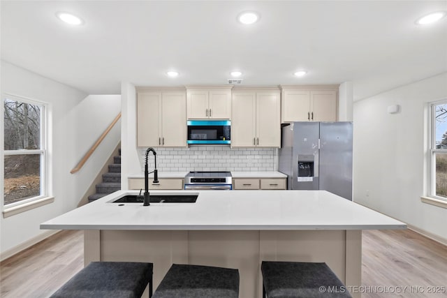 2002 W Driftwood Dr, Claremore, OK 74017 - kitchen featuring light wood-type flooring, appliances with stainless steel finishes, a kitchen island with sink, a sink, and decorative backsplash