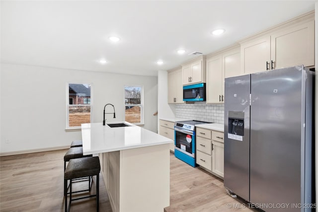 2002 W Driftwood Dr, Claremore, OK 74017 - kitchen featuring a sink, light wood-type flooring, appliances with stainless steel finishes, a kitchen island with sink, and backsplash