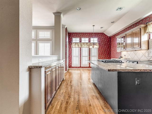 kitchen with glass insert cabinets, a notable chandelier, pendant lighting, wallpapered walls, and light wood-style flooring